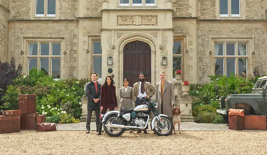 Royal Enfield Classic 350 Motorrad vor einem Herrenhaus, mit mehreren Personen und Reisegepäck