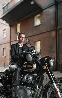 Fahrerin auf einer Royal Enfield Classic 650 Motorrad vor Backsteingebäude