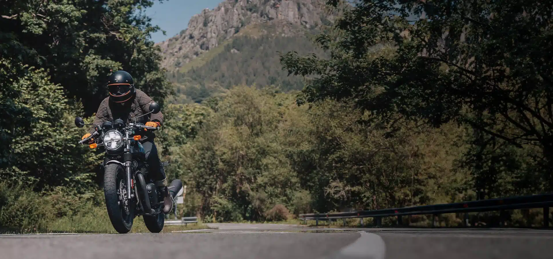 Motorradfahrer auf Royal Enfield Continental GT 650 auf offener Landstraße vor bewaldeten Bergen.