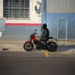 Motorradfahrer sitzt auf einer Royal Enfield Guerrilla 450 vor einer Halle in der Stadt.