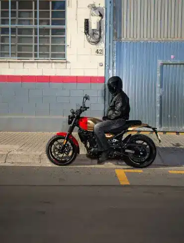 Motorradfahrer sitzt auf einer Royal Enfield Guerrilla 450 vor einer Halle in der Stadt.