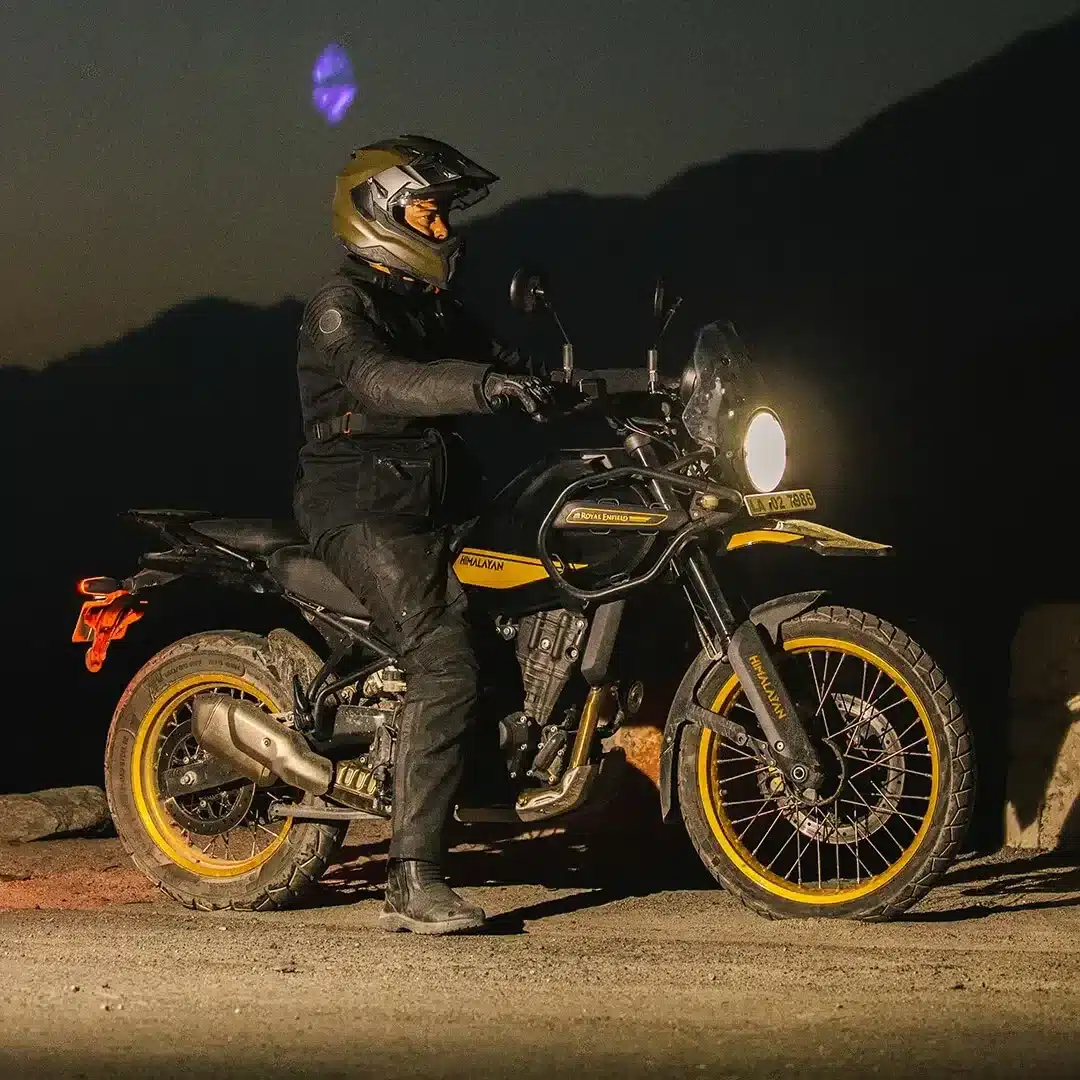 Royal Enfield Himalayan 450 Motorrad mit Fahrer bei Nacht auf einer Straße vor Bergen.
