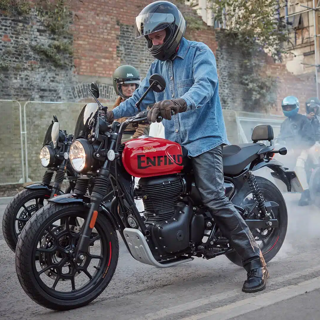 Motorradfahrer auf einer Royal Enfield HNTR 350 mit rotem Tank in einer urbanen Straßenszene