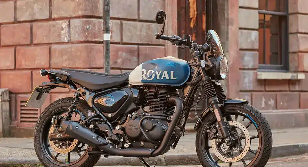Royal Enfield HNTR 350 Motorrad, blau-weiß, geparkt auf einer Straße vor Backsteingebäude