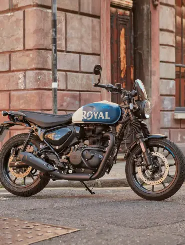 Royal Enfield HNTR 350 Motorrad, blau-weiß, geparkt auf einer Straße vor Backsteingebäude