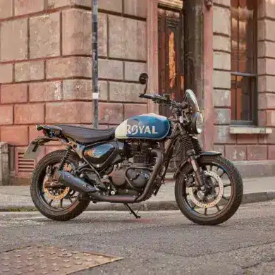 Royal Enfield HNTR 350 Motorrad, blau-weiß, geparkt auf einer Straße vor Backsteingebäude
