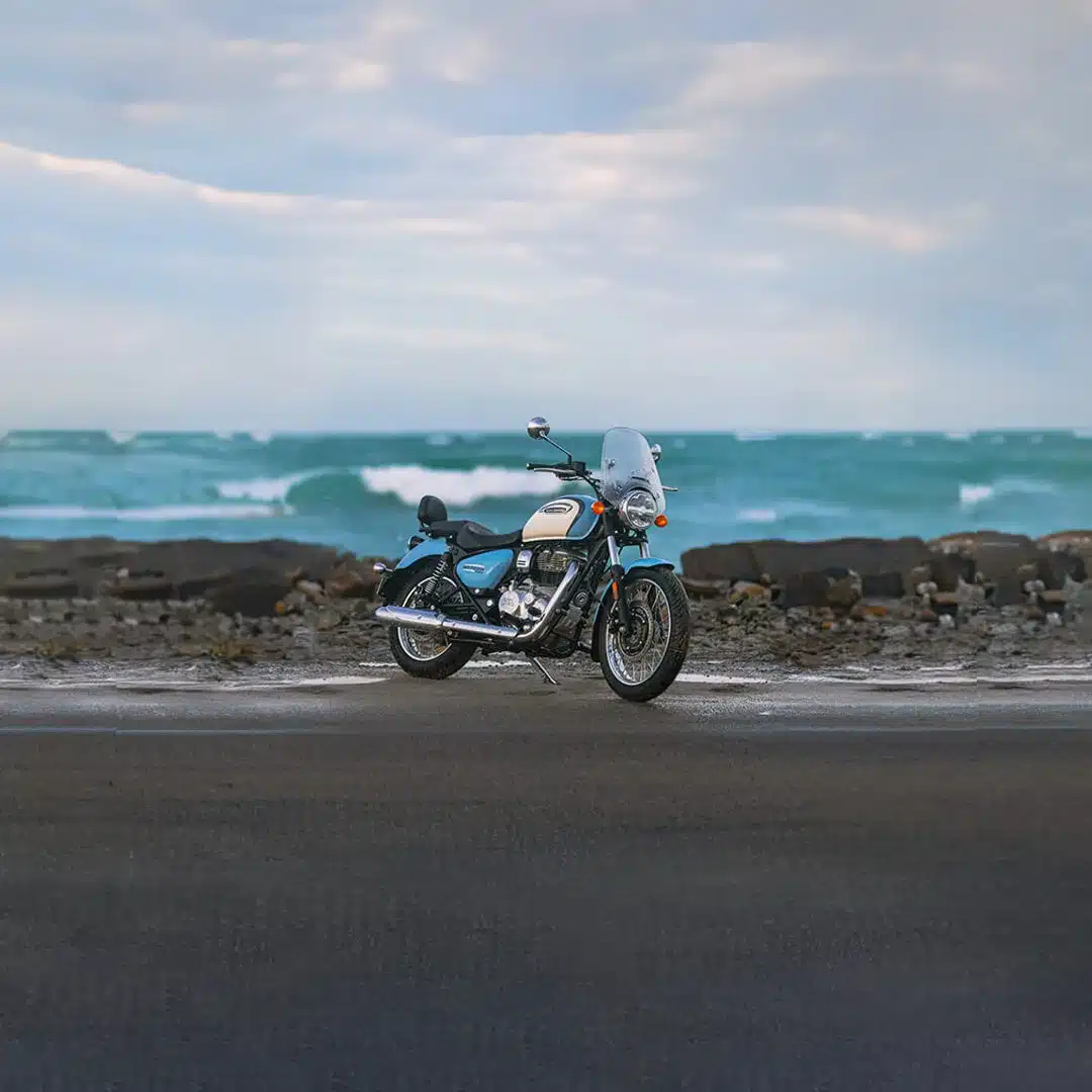 Royal Enfield Meteor 350 Aurora Blue geparkt am Meer, mit Felsen und Wellen im Hintergrund