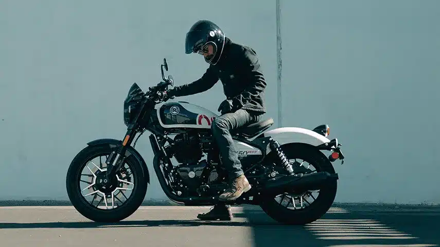 Motorradfahrer auf einer weißen Royal Enfield Shotgun 650 vor einer hellen Wand.