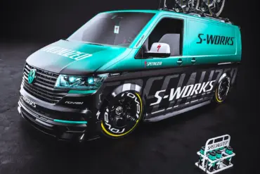 VW Transporter mit Specialized S-Works-Folierung, blauen und schwarzen Akzenten, RAYS TE37 Felgen und zwei Rennrädern auf dem Dachträger.