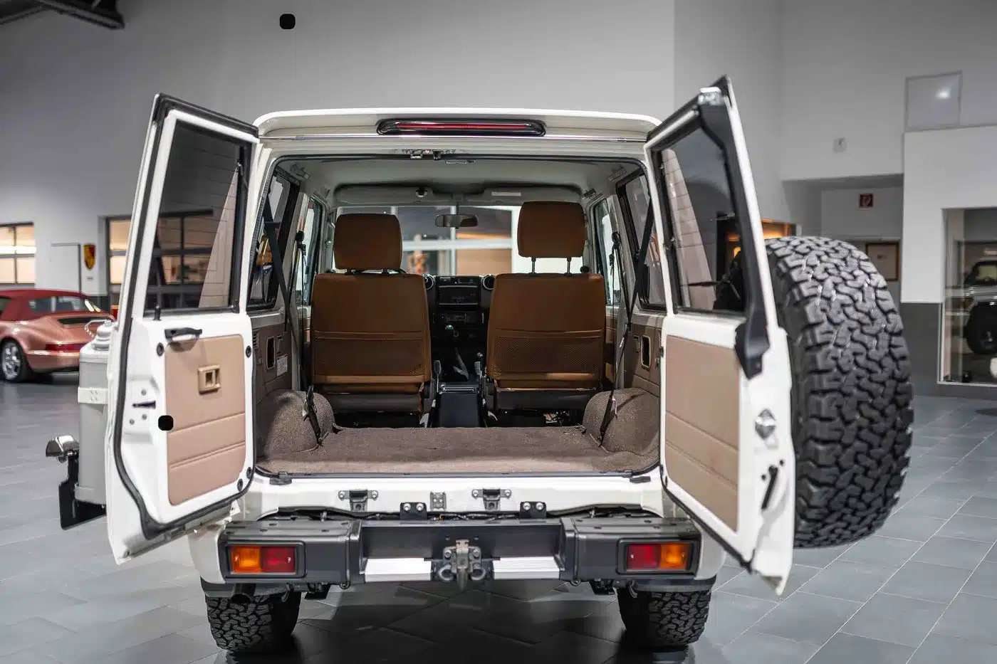 Geöffneter Laderaum eines weißen Toyota Land Cruiser 70 Jahre Edition mit braunen Sitzen und Ersatzrad an der Hecktür.