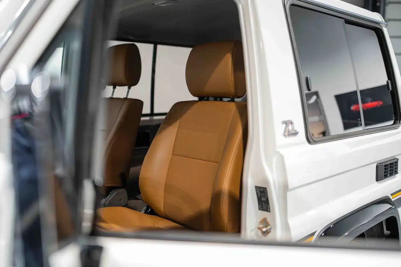 Braune Ledersitze und geöffnete Tür im weißen Toyota Land Cruiser 70 Jahre Edition, Innenraumdetail.