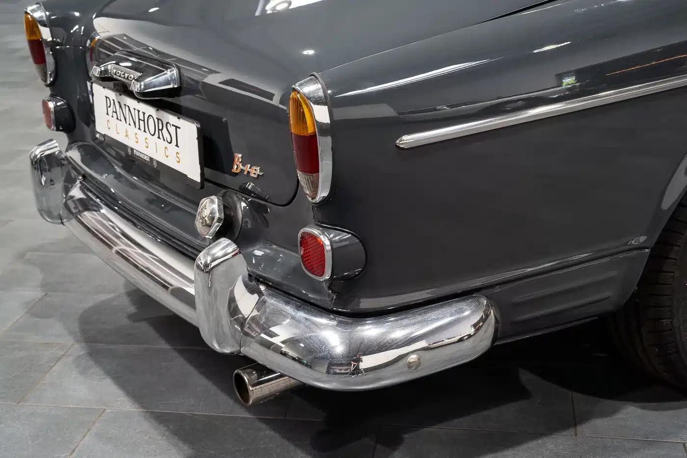Rückansicht eines dunkelgrauen Volvo Amazon Coupé mit Chromstoßfänger und Rückleuchten, aufgenommen in einer Halle.