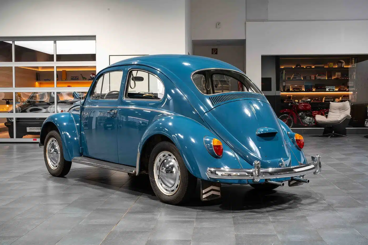 Blauer VW Käfer 1200 von 1964 aus schräger Heckansicht in einer modernen Ausstellungshalle.
