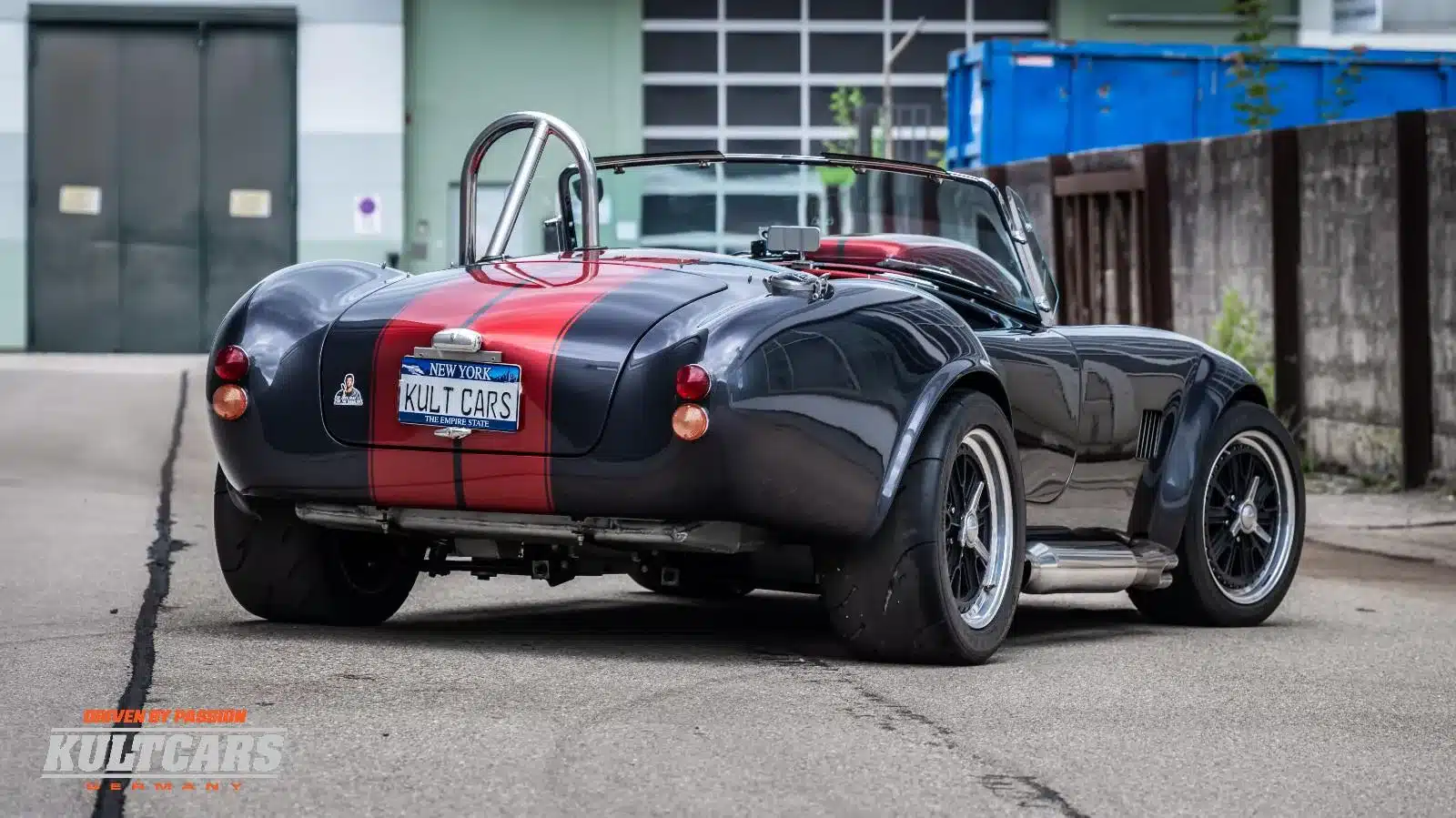 Rückansicht einer grauen Weineck Cobra 10.2L mit roten Streifen und offenem Verdeck auf einer Straße.