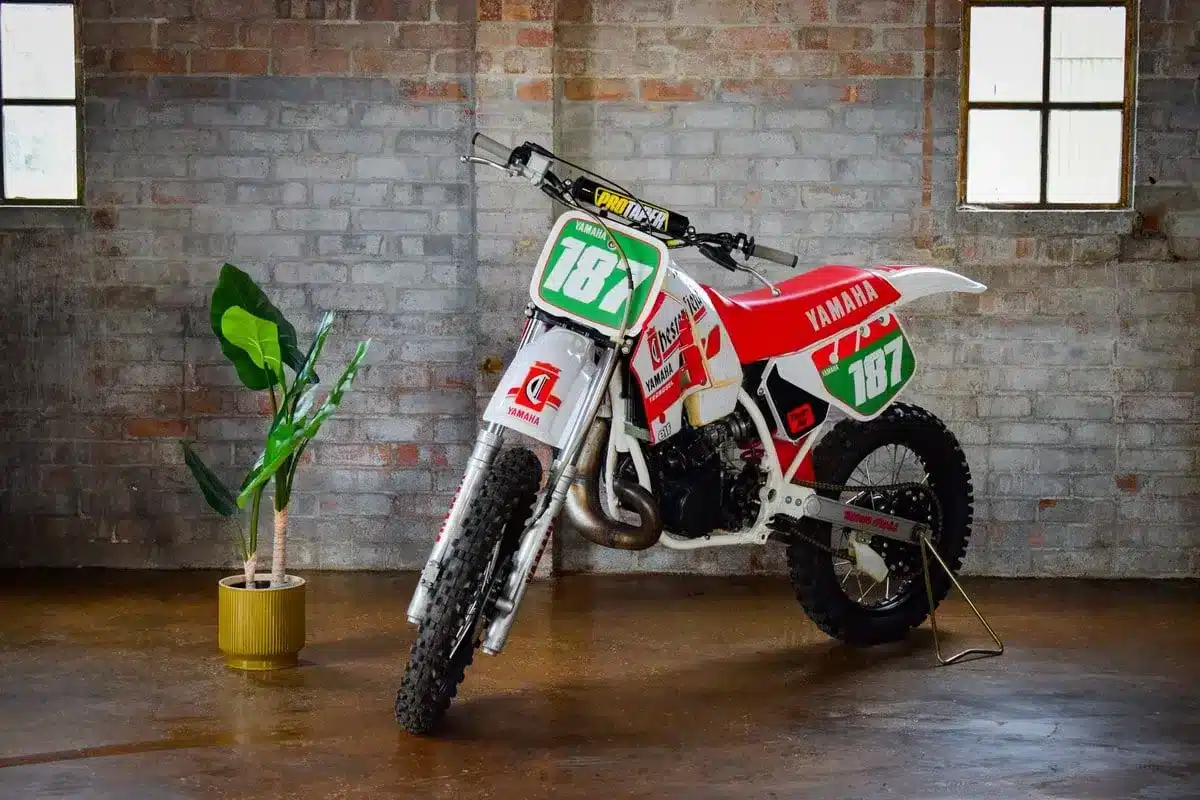 Yamaha YZ250 von 1987 in weiß-rotem Chesterfield-Design vor Backsteinwand, Seitenansicht.