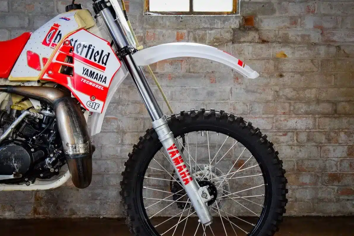 Yamaha YZ250 von 1987 im Chesterfield-Look, Detailansicht des Vorderrads und Rahmens vor einer Backsteinwand