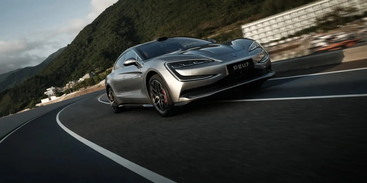 Silberner YangWang U7 fährt auf einer kurvigen Bergstraße, im Vordergrund die markante Front des Flaggschiffs, umgeben von grüner Hügellandschaft.