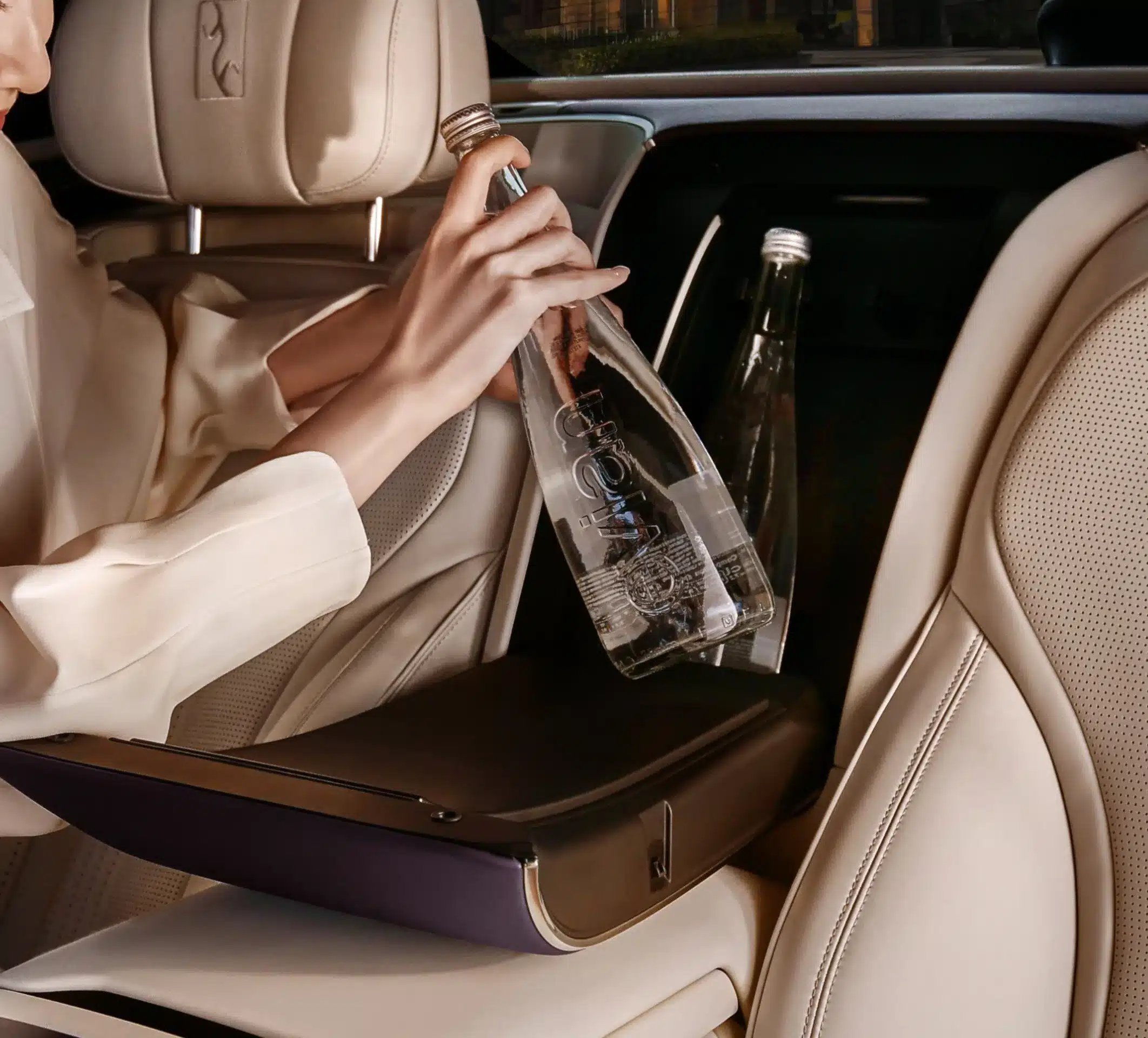 Luxuriöser Innenraum eines YangWang U7 mit hellen Ledersitzen und integrierter Getränkeablage, in die eine Person eine Wasserflasche stellt.