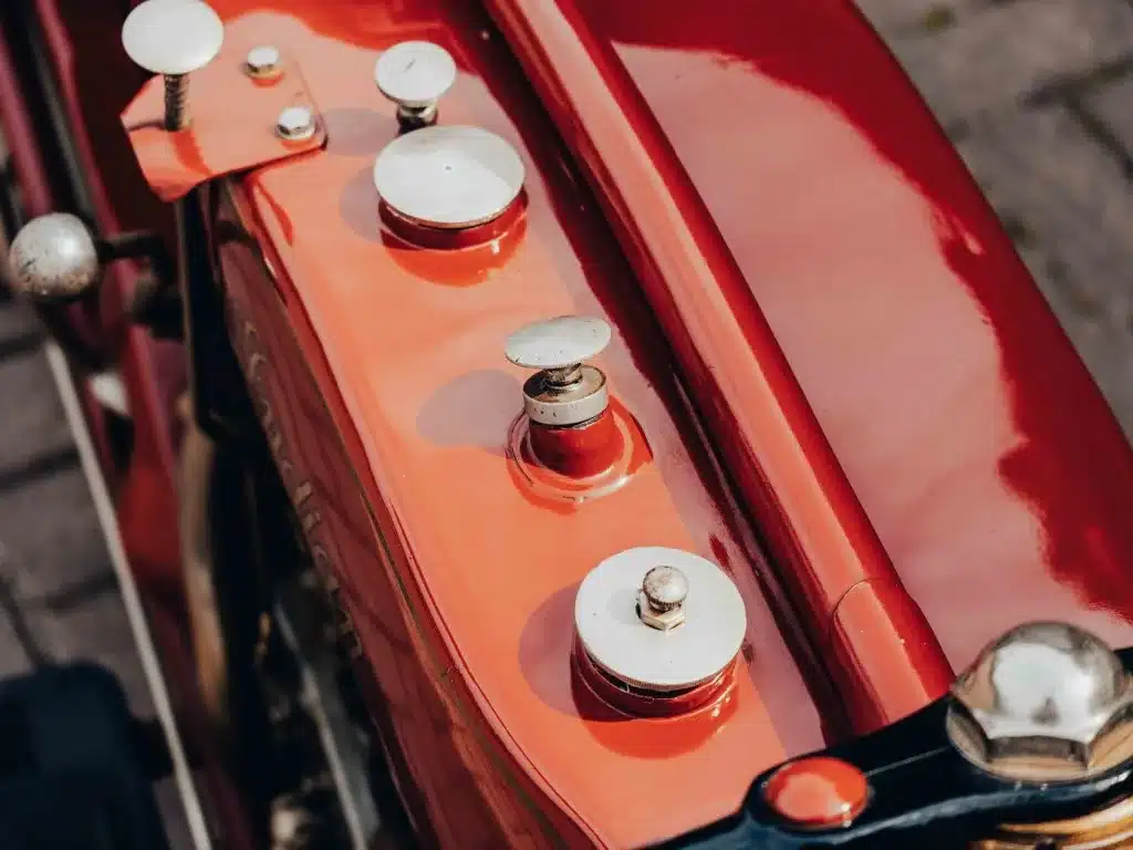 Detailansicht des rot lackierten Tanks der 1925 Indian Scout mit mehreren Tankdeckeln und Bedienelementen.