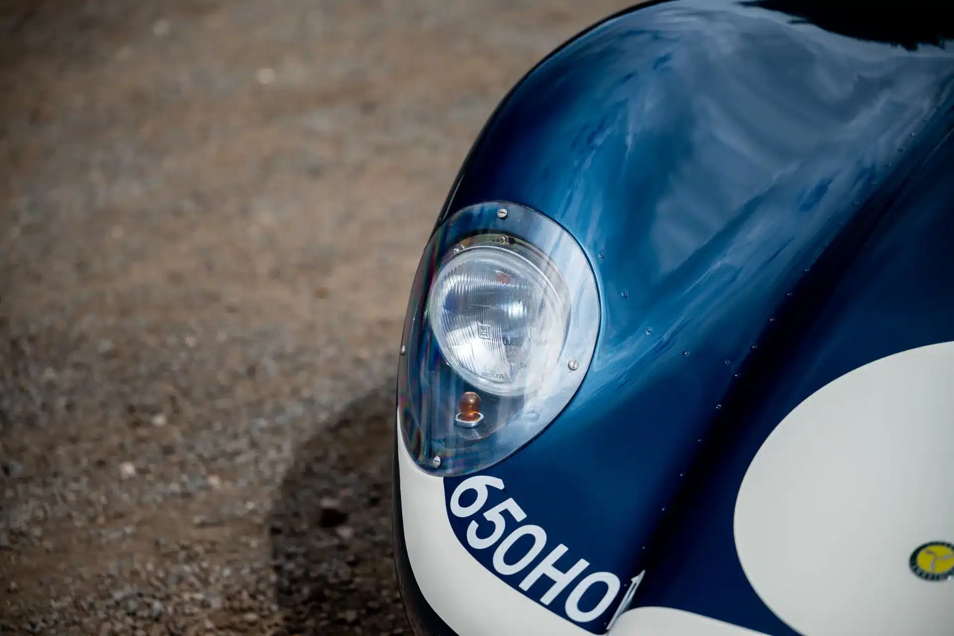 Detailaufnahme vom Frontscheinwerfer und Aluminiumblech des Lister-Jaguar Knobbly, lackiert in Blau mit weißem Rundfeld und Kennzeichen 650 HOD.