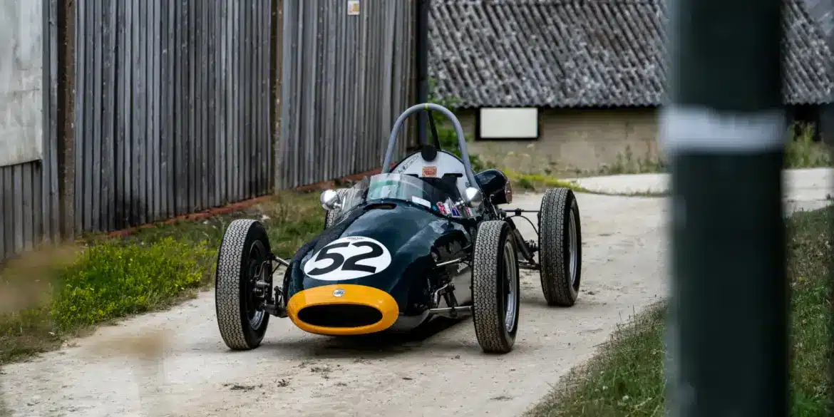 Historischer Cooper BMC T52 Formel-Junior-Rennwagen von 1960 mit Startnummer 52, dunkelgrün mit gelber Front, auf einem Kiesweg abgestellt.