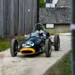 Historischer Cooper BMC T52 Formel-Junior-Rennwagen von 1960 mit Startnummer 52, dunkelgrün mit gelber Front, auf einem Kiesweg abgestellt.