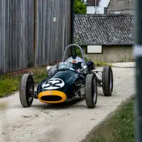 Historischer Cooper BMC T52 Formel-Junior-Rennwagen von 1960 mit Startnummer 52, dunkelgrün mit gelber Front, auf einem Kiesweg abgestellt.