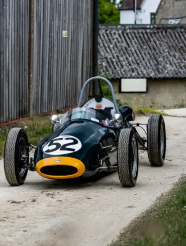 Historischer Cooper BMC T52 Formel-Junior-Rennwagen von 1960 mit Startnummer 52, dunkelgrün mit gelber Front, auf einem Kiesweg abgestellt.