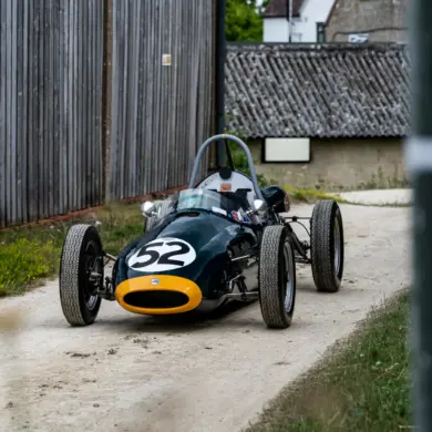 Historischer Cooper BMC T52 Formel-Junior-Rennwagen von 1960 mit Startnummer 52, dunkelgrün mit gelber Front, auf einem Kiesweg abgestellt.