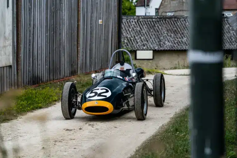 Historischer Cooper BMC T52 Formel-Junior-Rennwagen von 1960 mit Startnummer 52, dunkelgrün mit gelber Front, auf einem Kiesweg abgestellt.