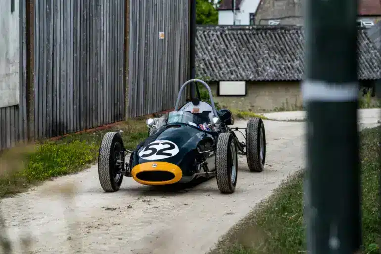 Historischer Cooper BMC T52 Formel-Junior-Rennwagen von 1960 mit Startnummer 52, dunkelgrün mit gelber Front, auf einem Kiesweg abgestellt.