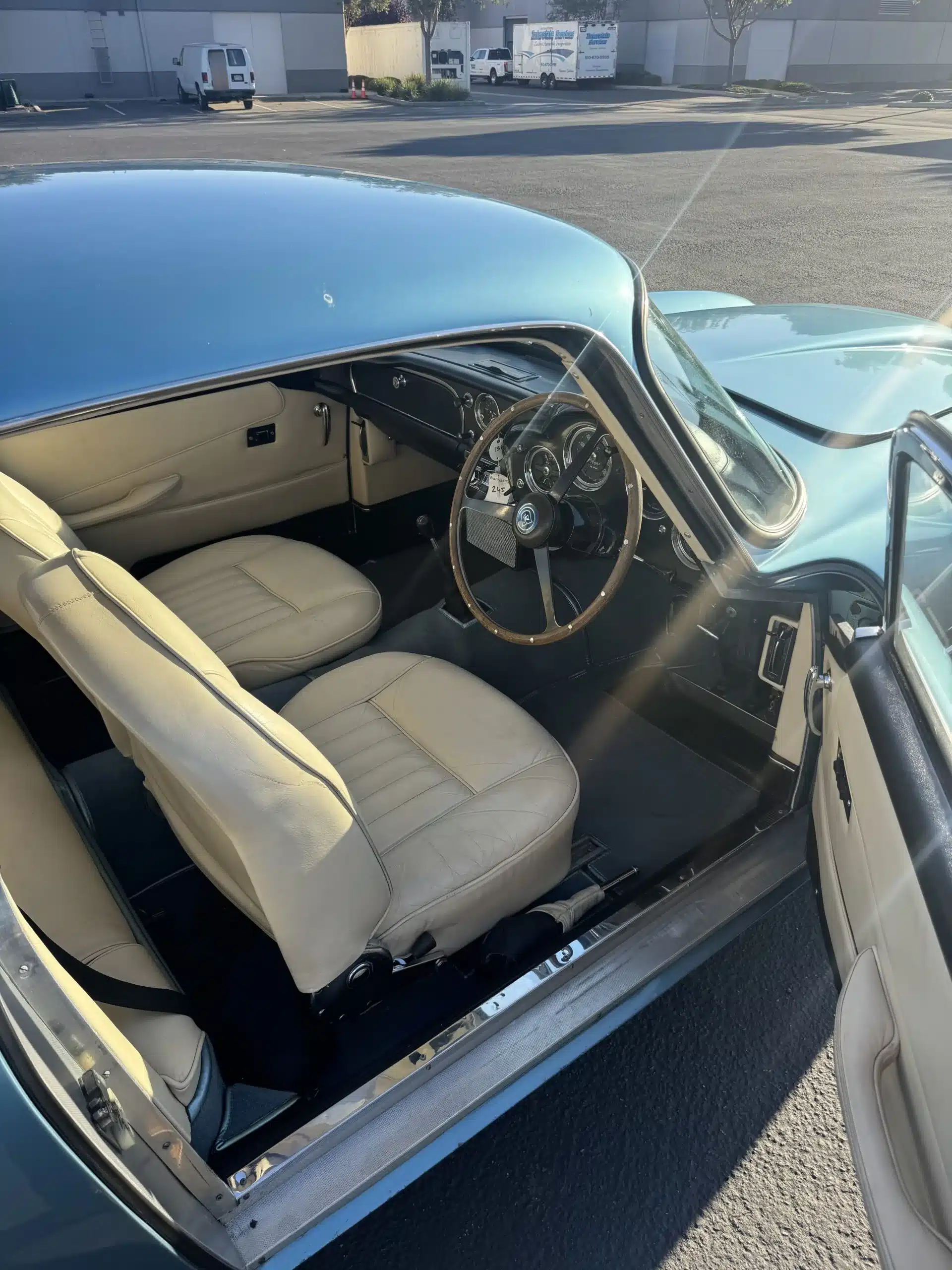 Innenansicht eines 1961 Aston Martin DB4 Vantage mit hellem Leder und Holzlenkrad, Fahrersitz auf der rechten Seite.