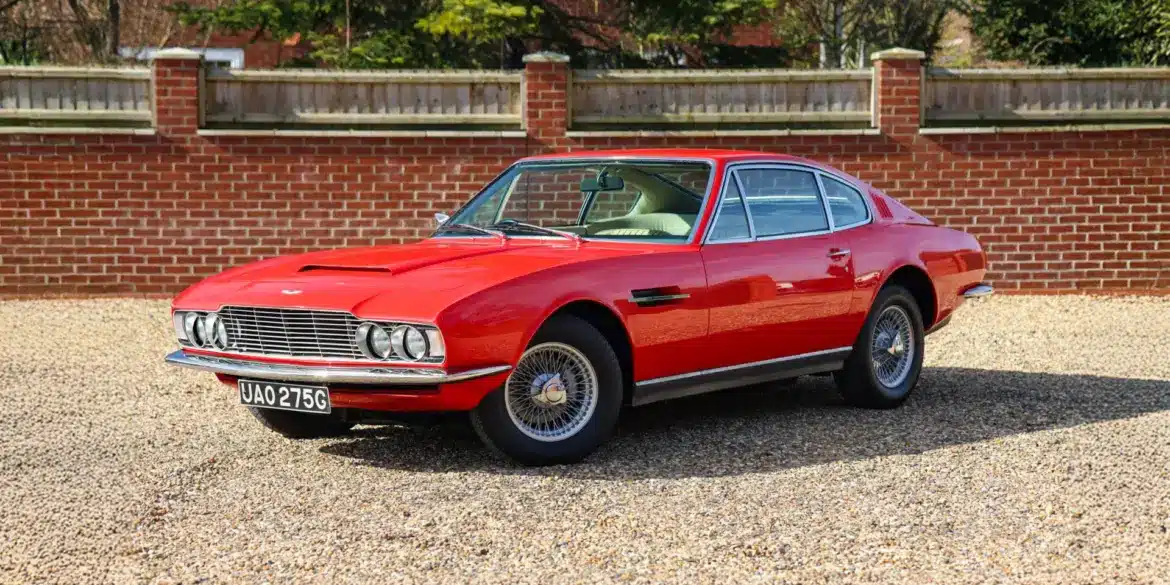 Roter Aston Martin DBS von 1969 mit beigem Leder, aufgenommen im Stand vor einer Ziegelmauer.