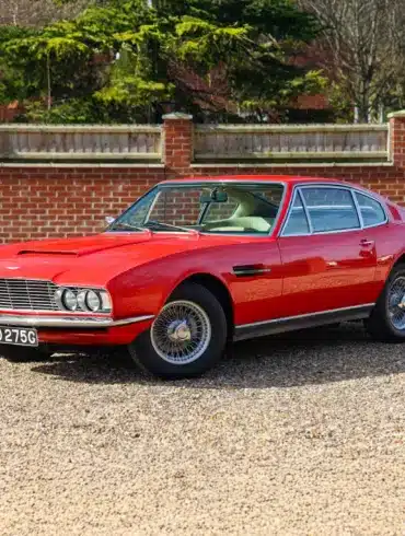 Roter Aston Martin DBS von 1969 mit beigem Leder, aufgenommen im Stand vor einer Ziegelmauer.