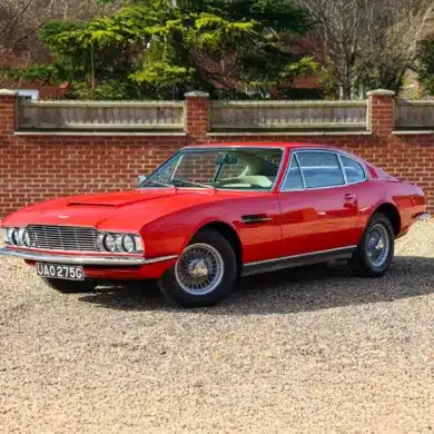 Roter Aston Martin DBS von 1969 mit beigem Leder, aufgenommen im Stand vor einer Ziegelmauer.