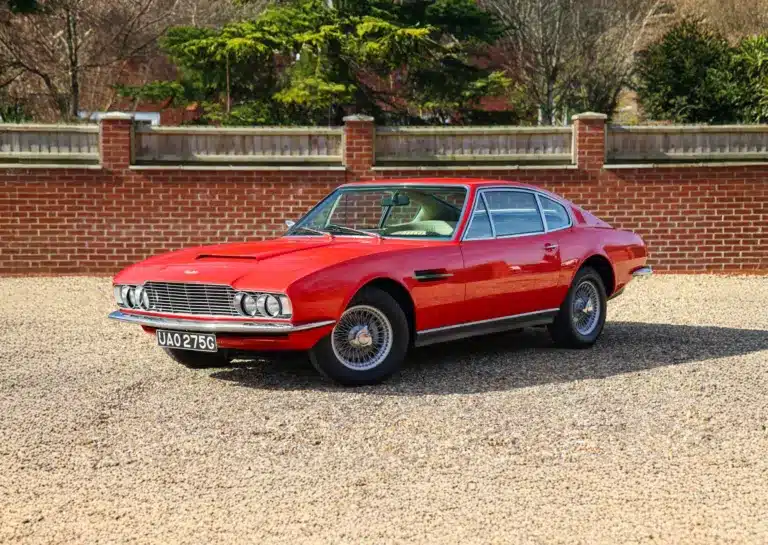 Roter Aston Martin DBS von 1969 mit beigem Leder, aufgenommen im Stand vor einer Ziegelmauer.