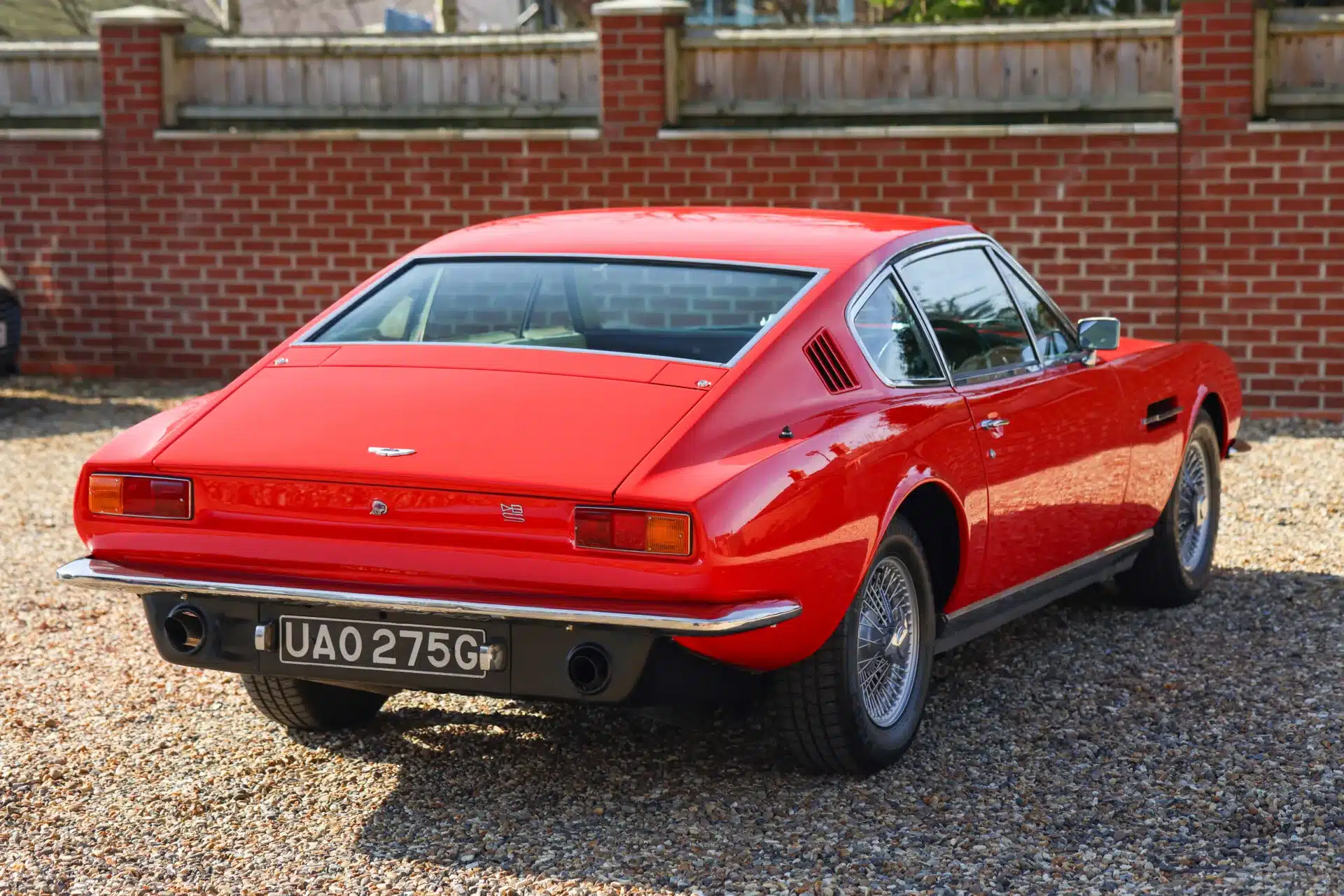 Roter Aston Martin DBS Baujahr 1969, von hinten fotografiert, auf Kies vor einer Ziegelmauer.