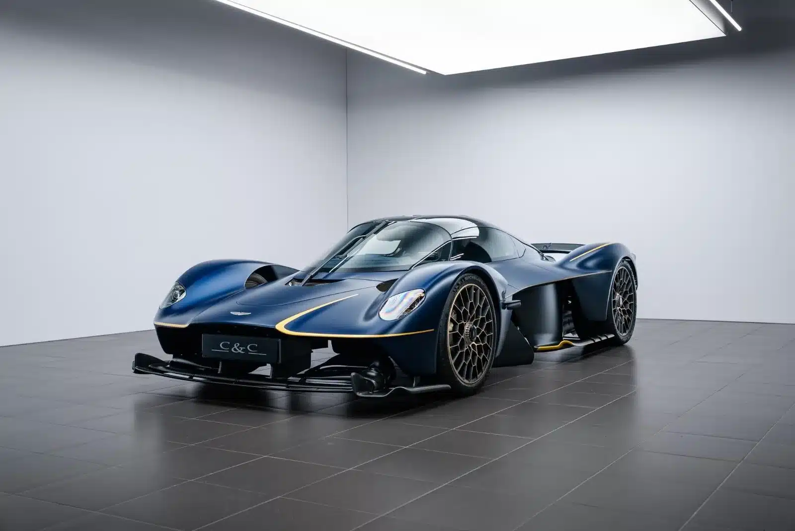 Aston Martin Valkyrie in blauer Lackierung mit goldenen Akzenten, aufgenommen im Innenraum eines Showrooms