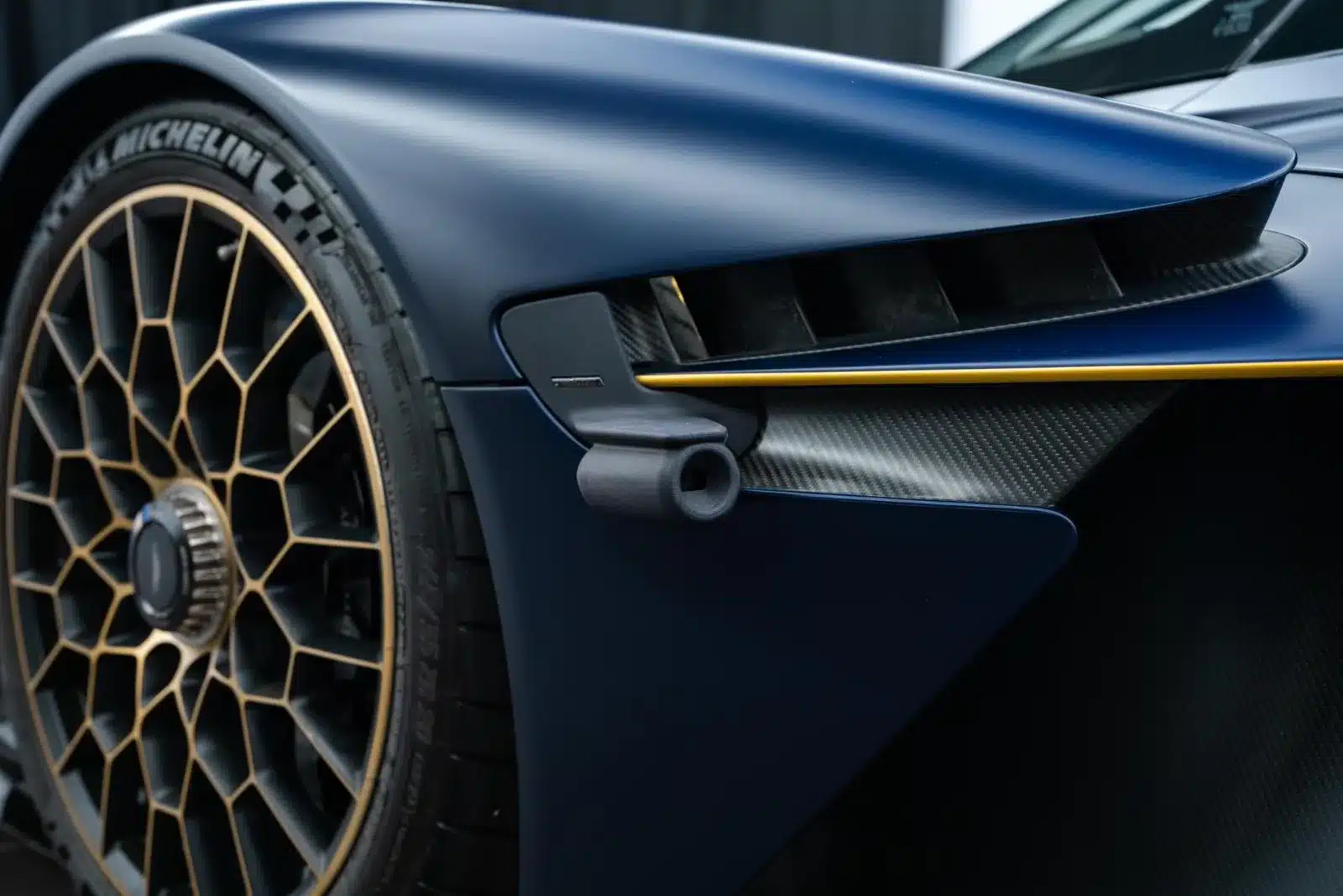 Detailansicht des Aston Martin Valkyrie mit Fokus auf das goldene Felgendesign, Reifentextur und Karbon-Elemente der vorderen Karosserie.