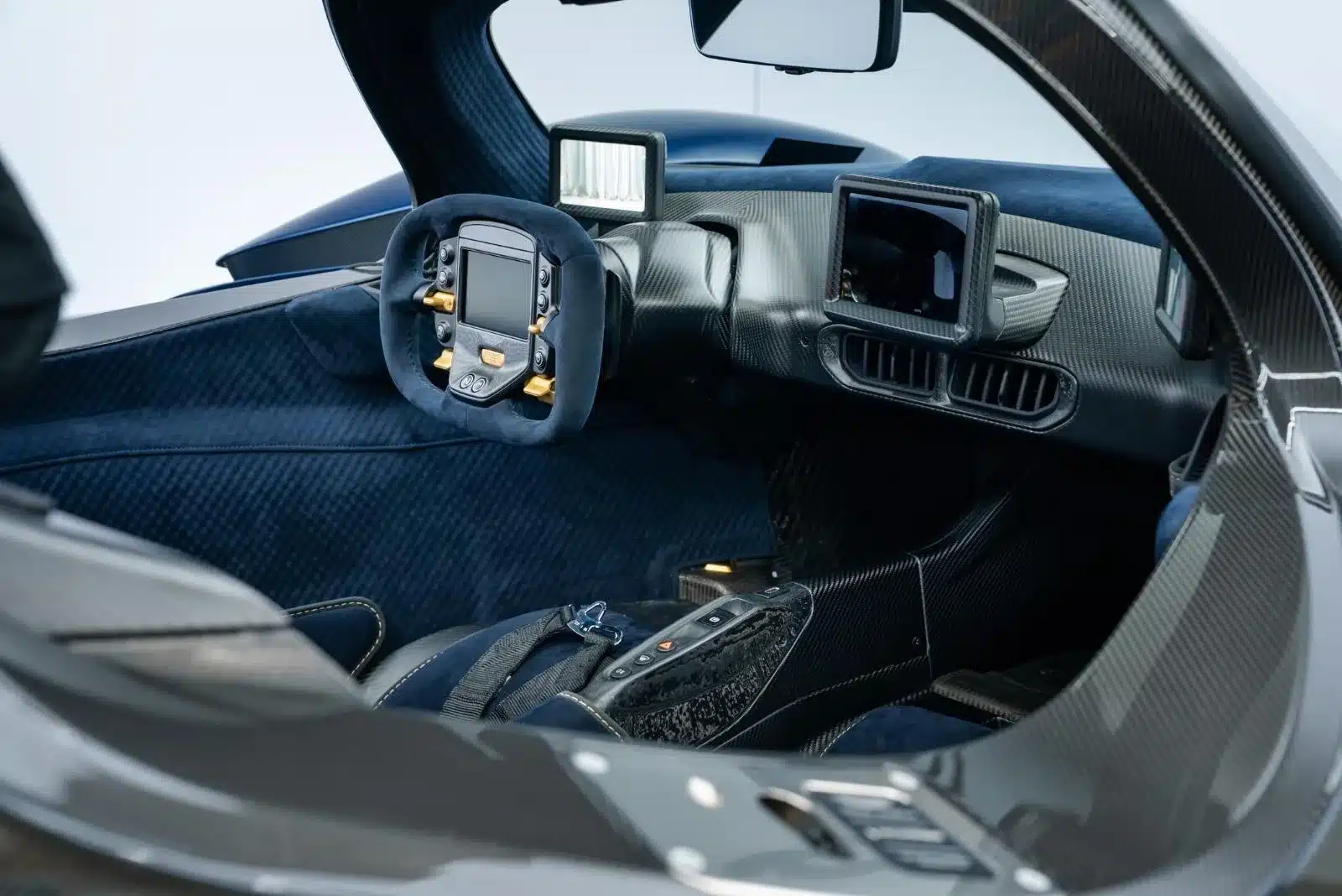 Innenraum eines Aston Martin Valkyrie mit Lenkrad und digitalen Anzeigen, hochwertige Carbon- und Alcantara-Ausstattung.