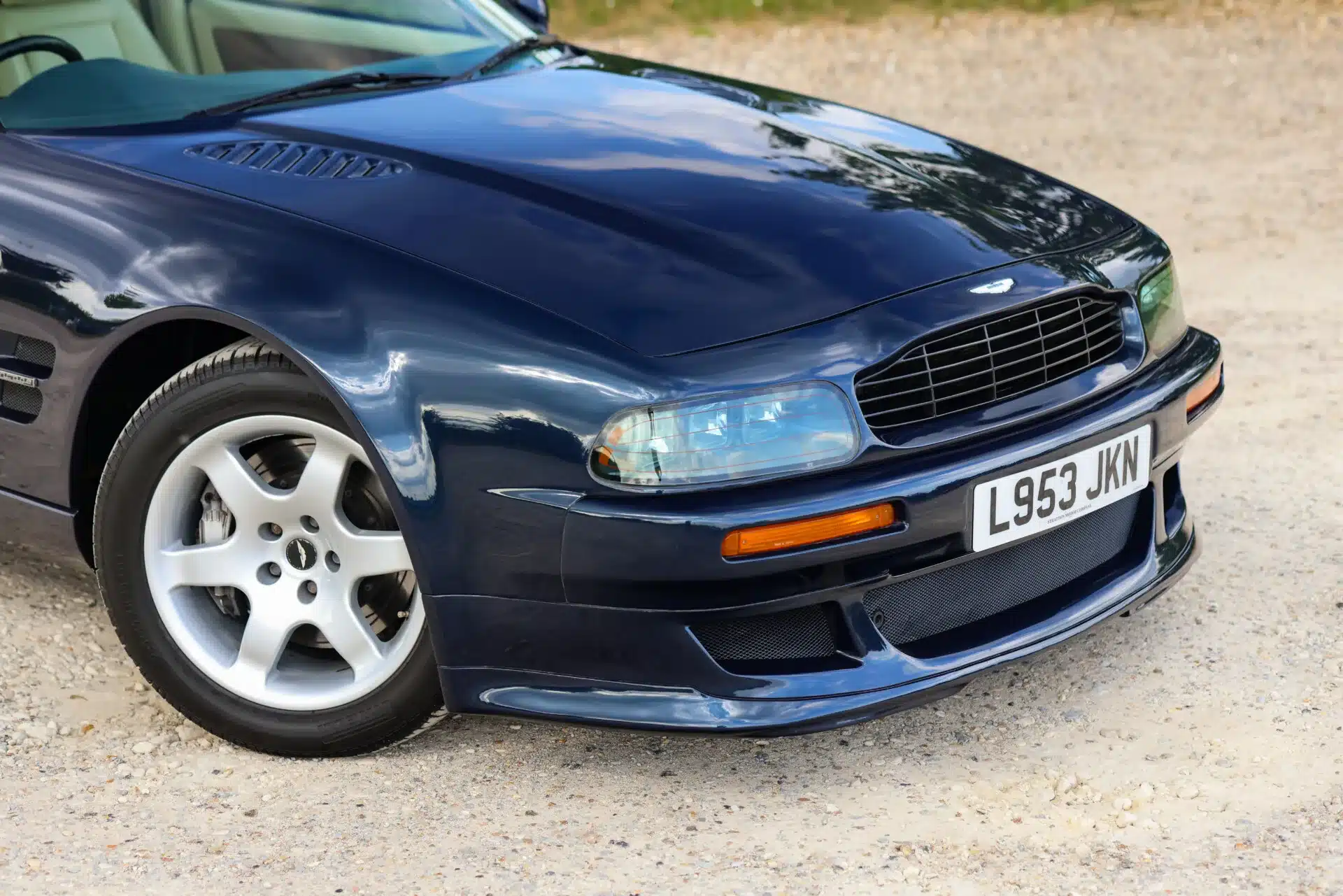 Frontansicht eines Aston Martin Vantage V550 in dunkelblau mit Aluminiumkarosserie und Scheinwerfern, stehend auf Kies.