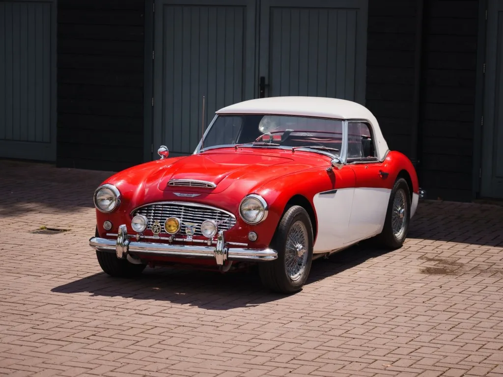 Austin-Healey 3000 MK1 BT7 von 1959 mit roter Lackierung, weißem Werks-Hardtop und Drahtspeichenrädern vor Garage