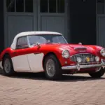 Austin-Healey 3000 MK1 BT7, Baujahr 1959, mit roter Lackierung und weißem Werks-Hardtop, von schräg vorne fotografiert.