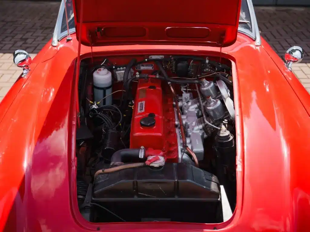 Offener Motorraum eines roten Austin-Healey 3000 MK1 BT7 mit sichtbarem Reihensechszylinder und SU-Vergasern.