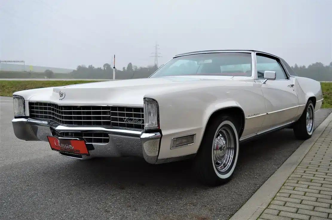 Frontansicht eines weißen Cadillac Eldorado Coupe 1969 mit schwarzem Vinyl-Dach und Chromrädern, geparkt auf einem Straßenrand
