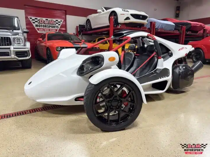 Weißer Campagna T‑Rex RR 2025 Dreirad mit Überrollkäfig, offener Sitzanordnung und sportlichem Design in einer Fahrzeughalle.