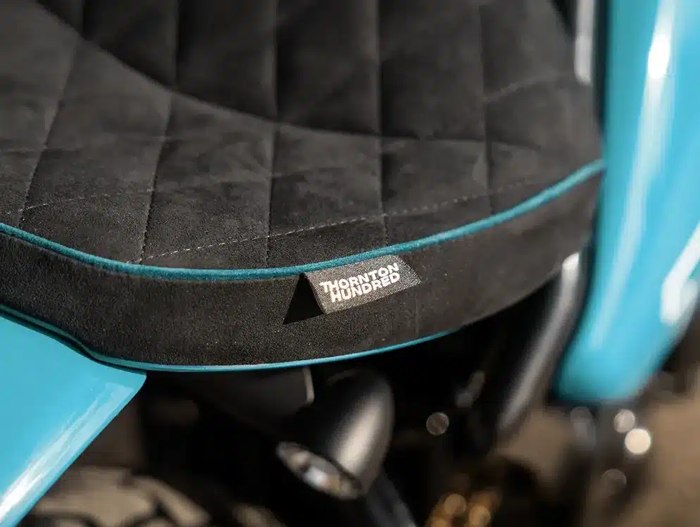 Nahaufnahme der handgefertigten, schwarz-blauen Sitzbank einer Thornton Hundred City Bobber mit gesticktem Thornton Hundred Markenetikett.