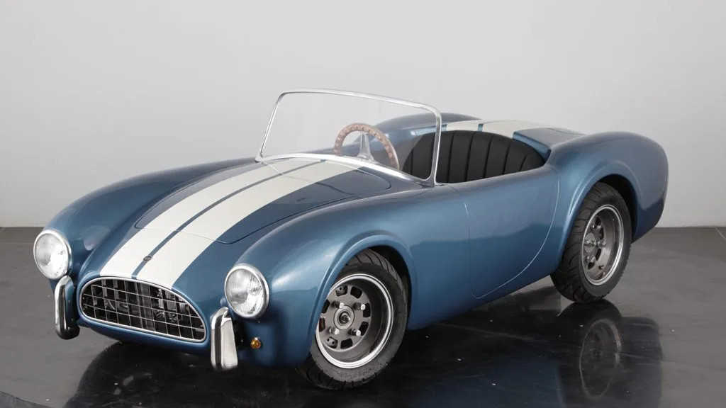 Cobra 289 Junior Kinderauto im Shelby-Blau mit weißen Rennstreifen, halbmaßstäblicher Roadster auf schwarzem Studiohintergrund.