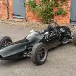 Cooper T59 Formula Junior Rennwagen von 1962 in dunkelgrüner Lackierung, frontal seitlich in einer Hofeinfahrt fotografiert.