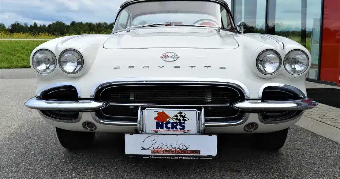 Weiße Corvette C1 Roadster 327 Dual Top, Baujahr 1962, von vorne aufgenommen, mit sichtbarem Emblem und Hardtop.